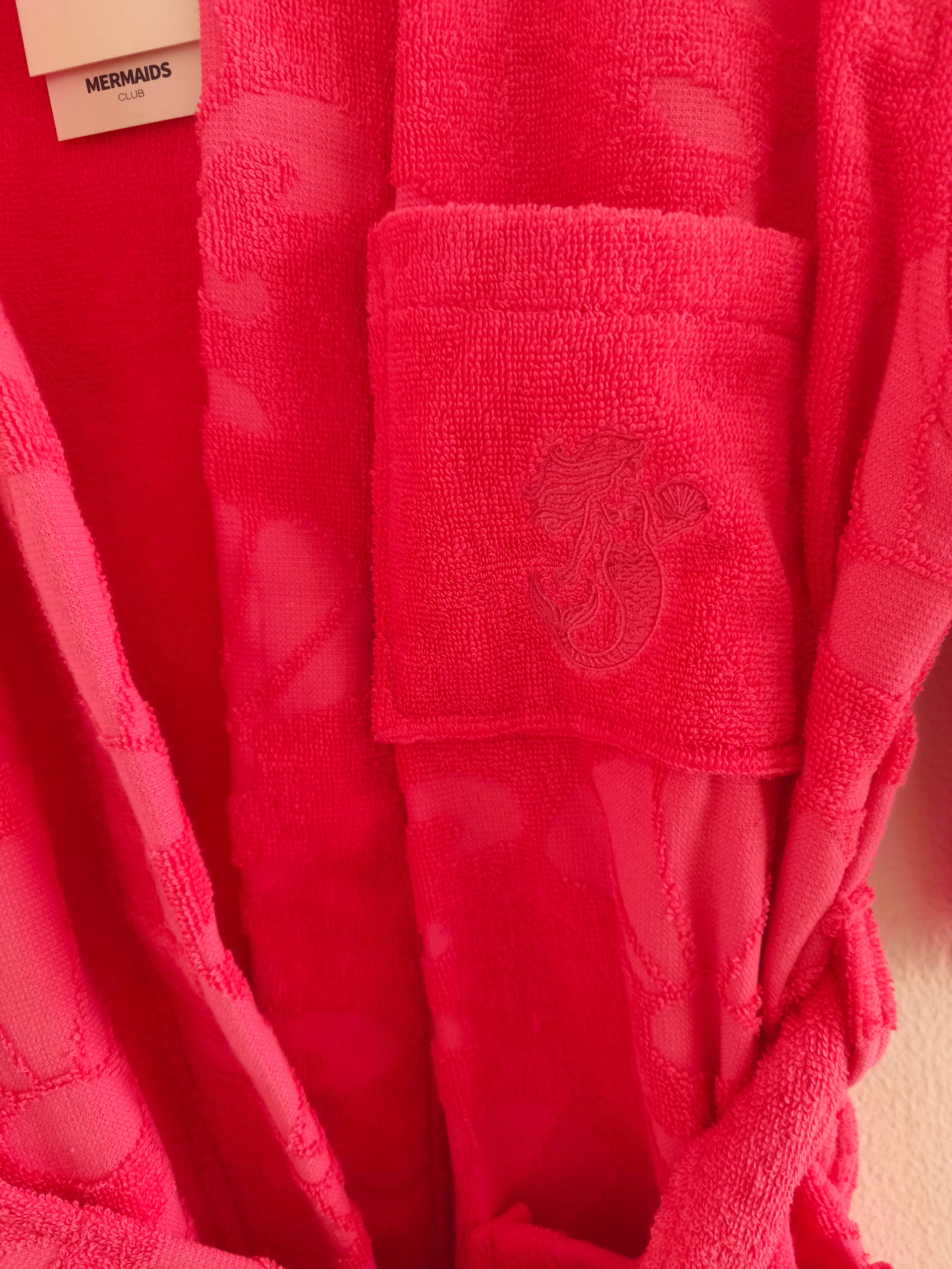 Close-up of a Mermaids Club Sunset Glow beachrobe with a logo emboidered on a pink red background